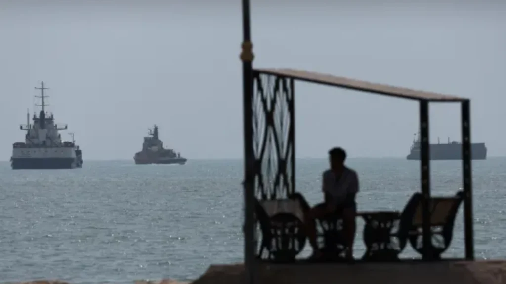 A person sitting on a seaside pavilion with ships anchored in the Gulf of Oman in the background.
