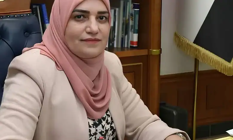 Iraqi woman wearing a pink hijab and beige blazer in an office setting.