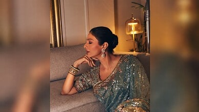 Tabu wearing a shimmering saree with jewelry, sitting thoughtfully on a sofa.