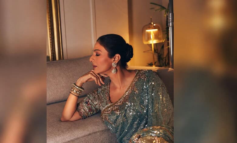 Tabu wearing a shimmering saree with jewelry, sitting thoughtfully on a sofa.