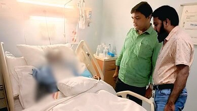 Two men standing beside a hospital bed with a blurred patient, in a medical setting in Saudi Arabia.