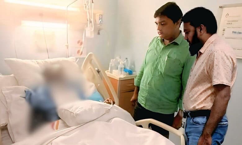 Two men standing beside a hospital bed with a blurred patient, in a medical setting in Saudi Arabia.