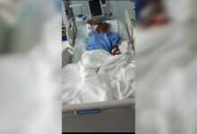 Injured worker lying in hospital bed with bandages and IV drip in hospital room.