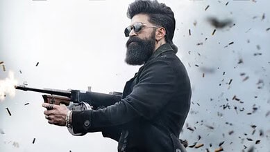 Man with a beard and sunglasses firing a gun amidst flying debris.