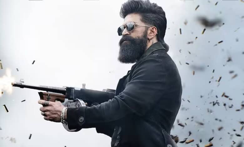 Man with a beard and sunglasses firing a gun amidst flying debris.
