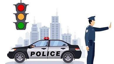 Traffic police officer signaling "stop" with hand, standing beside a police car with a traffic light and city skyline in the background.