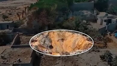 Large crater in the ground from a recent explosion, surrounded by damaged structures and debris.
