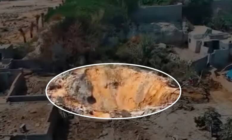 Large crater in the ground from a recent explosion, surrounded by damaged structures and debris.