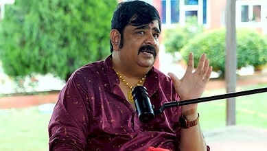 Astrologer Venu Swamy speaking outdoors with a microphone, gesturing with his hand.