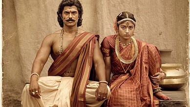 Actors in traditional Indian costumes for a film scene, seated on a stone platform.