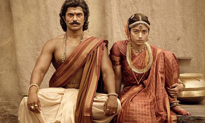 Actors in traditional Indian costumes for a film scene, seated on a stone platform.