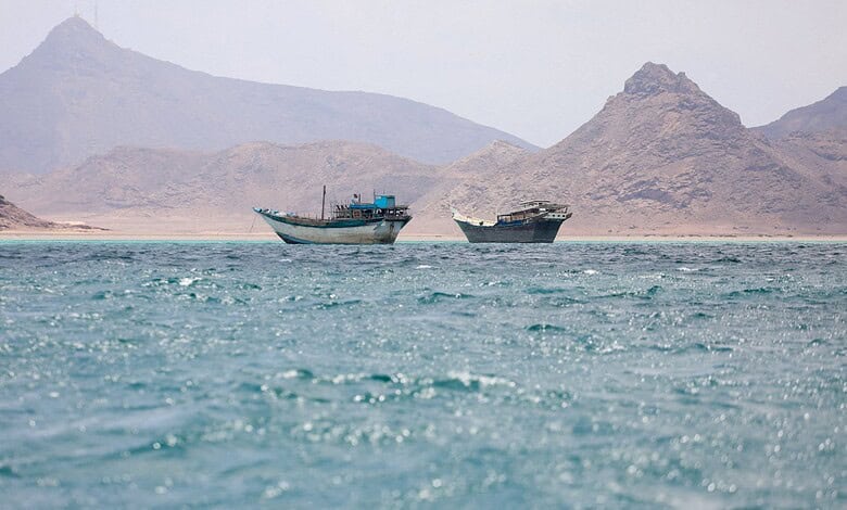 Two boats in rough waters near mountainous coastline, Yemen, during daytime.