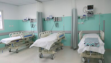 Empty hospital beds in a clean, well-equipped ward with medical monitors and curtains.