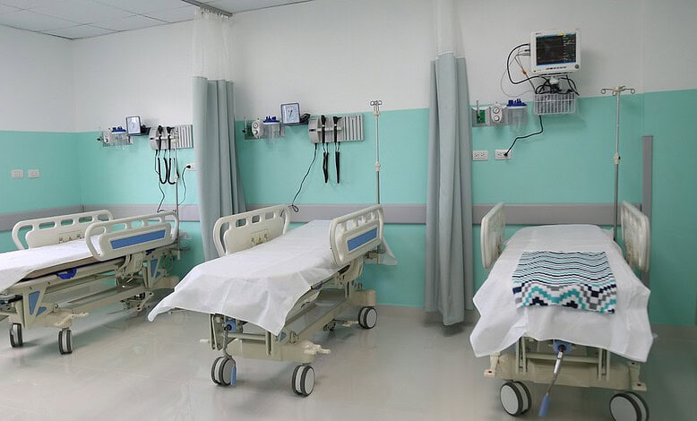 Empty hospital beds in a clean, well-equipped ward with medical monitors and curtains.