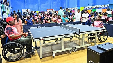 Wheelchair user playing table tennis at a busy indoor sports event in Hyderabad.