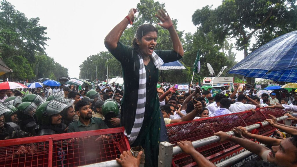 Protester passionately raises hands during a demonstration amid heavy rain and police presence.