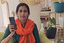 Woman holding a smartphone in a well-decorated room with plants and ornaments.