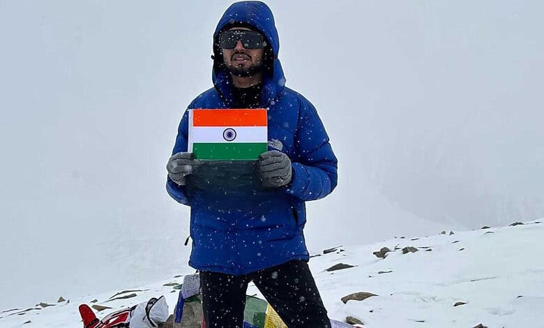 Man in blue jacket holding Indian flag on snowy mountain peak during daytime.