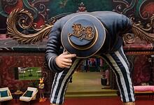 Person in Bigg Boss 20 house wearing a hat and striped pants, bowing down.