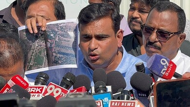 Indian politician speaking to media with microphones and reporters present.