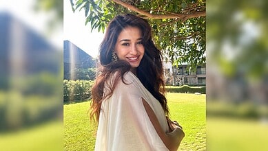 Disha Patani smiling outdoors in a beige outfit with greenery in the background.
