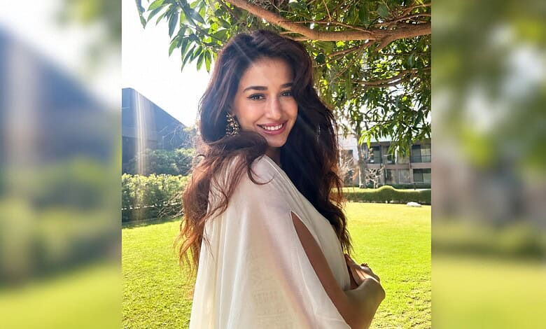Disha Patani smiling outdoors in a beige outfit with greenery in the background.