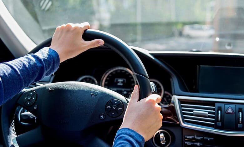 Close-up of a person holding a steering wheel inside a car during daytime.