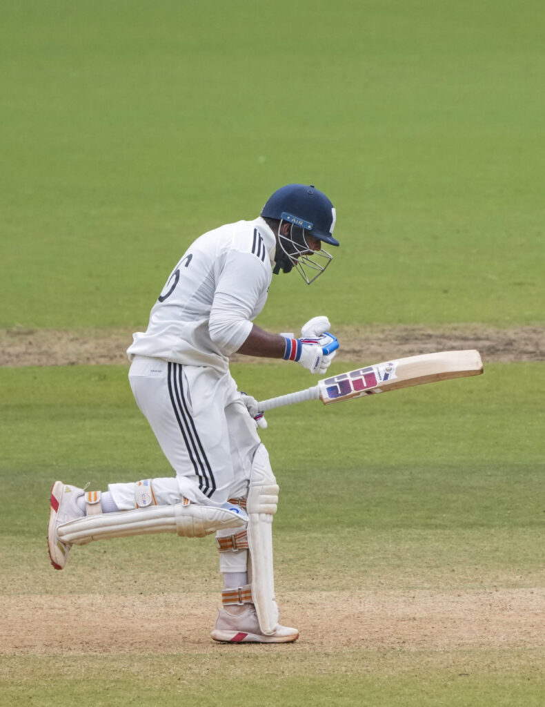 Cricketer running with bat and helmet on a cricket field during a match.