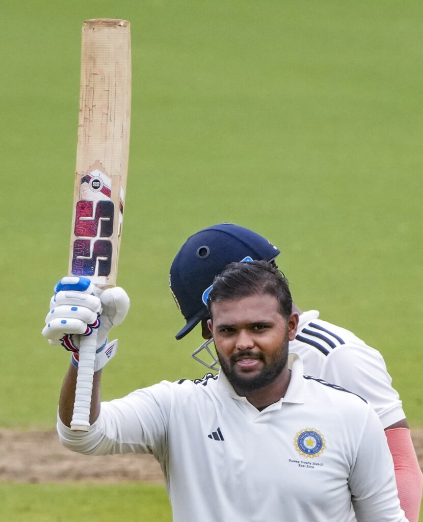 East Zone cricketer celebrates Duleep Trophy win after 13 years, holding bat aloft.