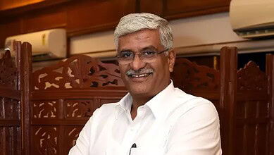 Shekhawat smiling in a formal setting, wearing a white shirt and glasses.
