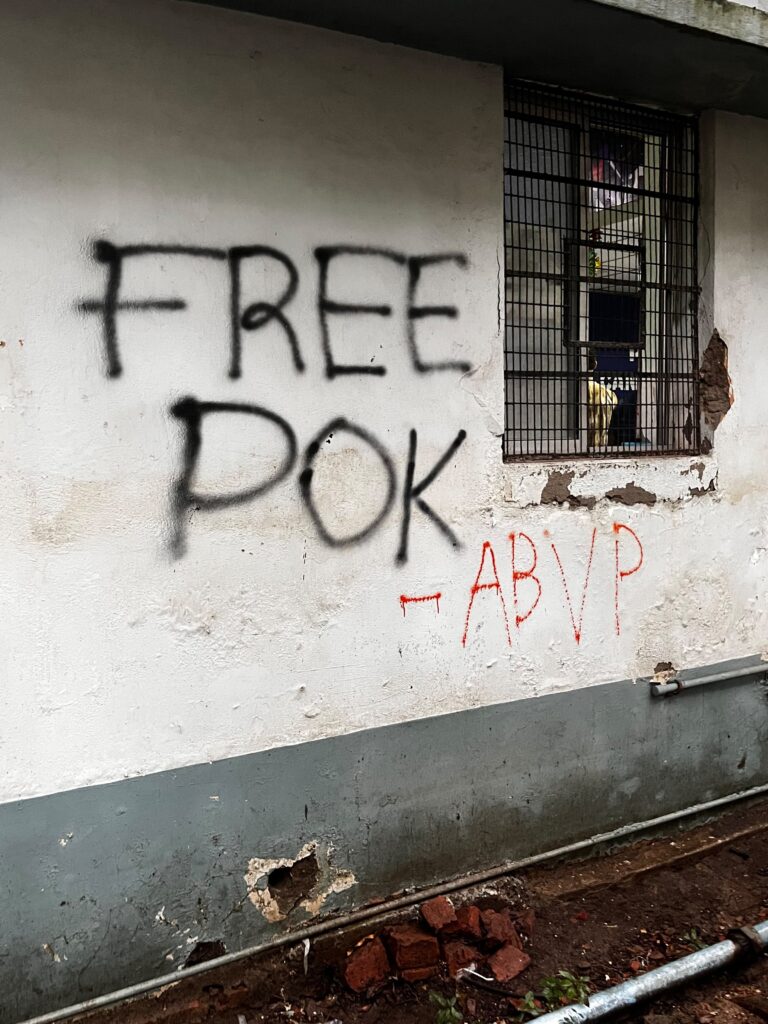 Graffiti on wall reading 'Free POK' with a barred window nearby.