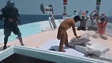 Authorities inspect large packages of seized drugs on a boat in the Arabian Sea with personnel and onlook.