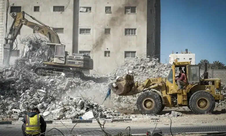 Bulldozers demolish rubble in Gaza, with workers observing the destruction.