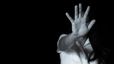 Child's hand raised in a stop gesture, black background, partial view of face and body.