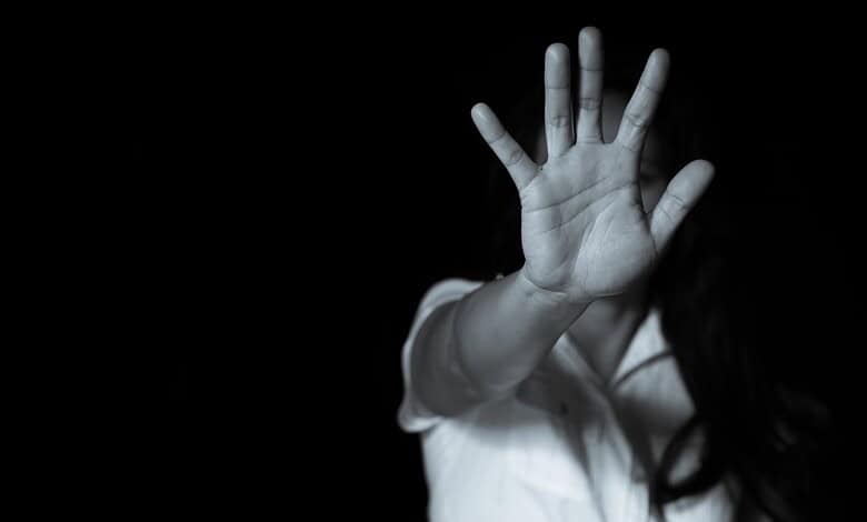 Child's hand raised in a stop gesture, black background, partial view of face and body.