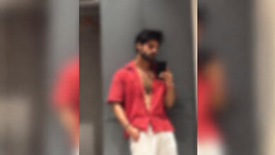 Person in red shirt and white pants taking a mirror selfie, wearing a face mask.