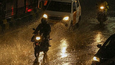 Motorcycles and cars navigating flooded streets during heavy monsoon rains in Hyderabad.