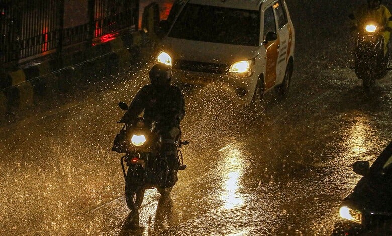 Motorcycles and cars navigating flooded streets during heavy monsoon rains in Hyderabad.