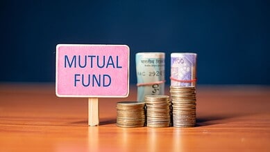 Stacks of Indian currency notes and coins with a 'Mutual Fund' sign on a wooden surface.