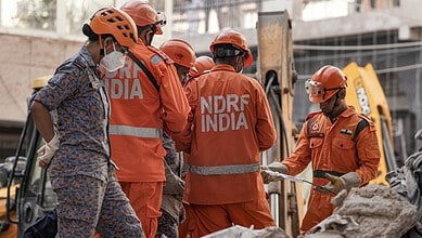 Rescue workers in orange uniforms and helmets at the site of a building collapse in Delhi.