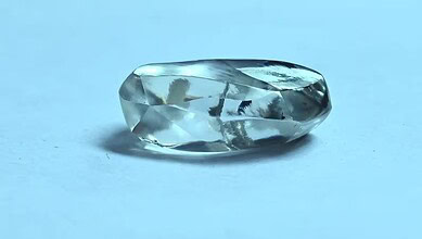 Close-up of a clear, faceted diamond on a light blue background.