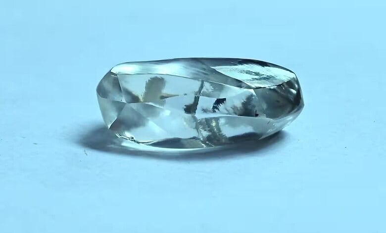 Close-up of a clear, faceted diamond on a light blue background.