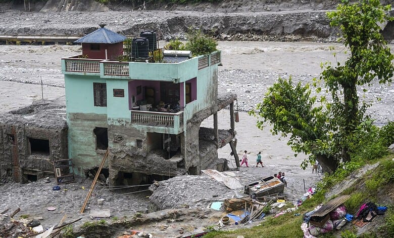 Flooded house in Nepal with debris and damaged vehicles after flash floods.