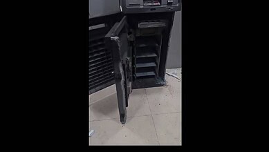 Damaged ATM machine with open cash compartment and debris on the floor.