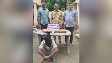 Three men standing behind a table with seized drugs, one man kneeling in front with face covered.