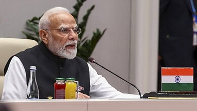 Indian Prime Minister Narendra Modi speaking at SCO summit with Indian flag on table.