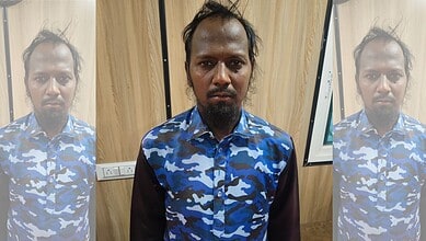 Man in blue camouflage shirt standing indoors with wooden wall background.
