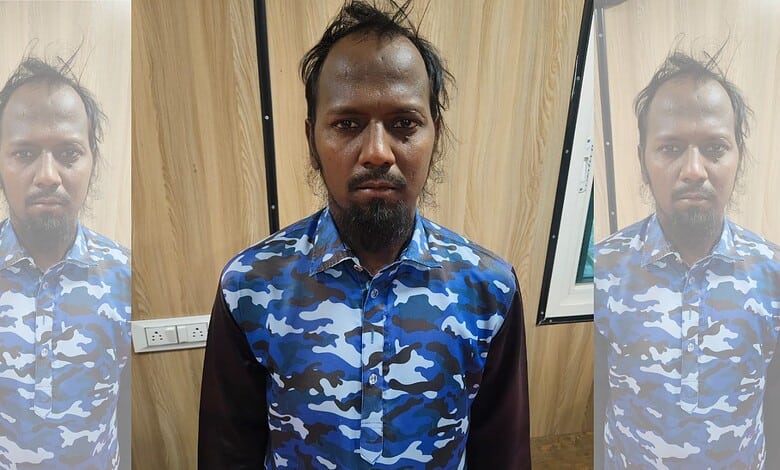 Man in blue camouflage shirt standing indoors with wooden wall background.