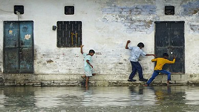 Children playing near the Ganga river in Varanasi, with a weathered wall in the background.
