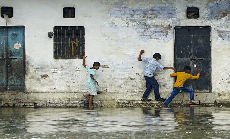 Children playing near the Ganga river in Varanasi, with a weathered wall in the background.